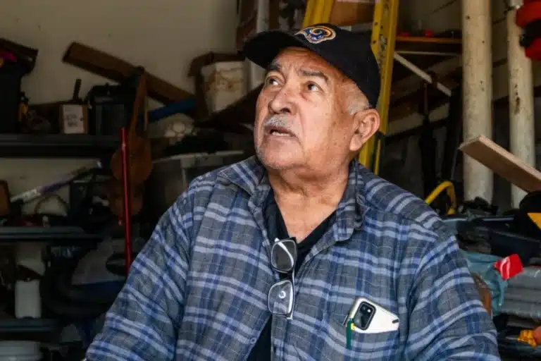 Elderly tenant in a cluttered garage looking upward with concern, representing residents displaced after a Mission District apartment fire and ongoing negligence lawsuit.