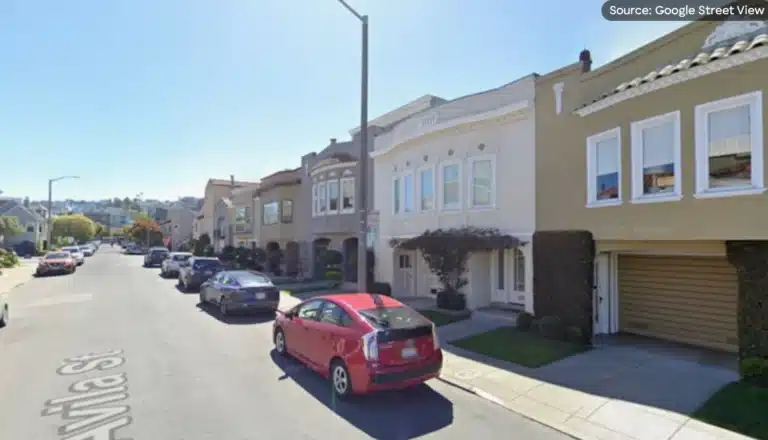 A street scene featuring parked cars alongside a house in the background.