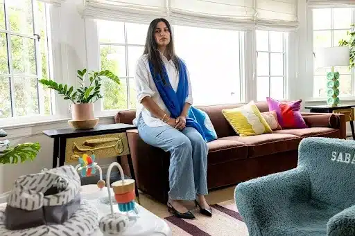 A woman sits comfortably on a couch in a cozy living room, surrounded by warm lighting and decorative elements.