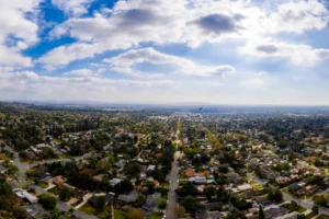 Aerial view of a bustling cityscape, showcasing buildings, streets, and green spaces under a clear blue sky.