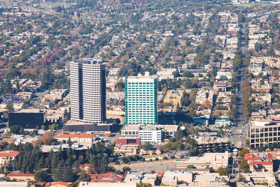 Aerial view of a bustling cityscape, showcasing buildings, streets, and green spaces under a clear blue sky.