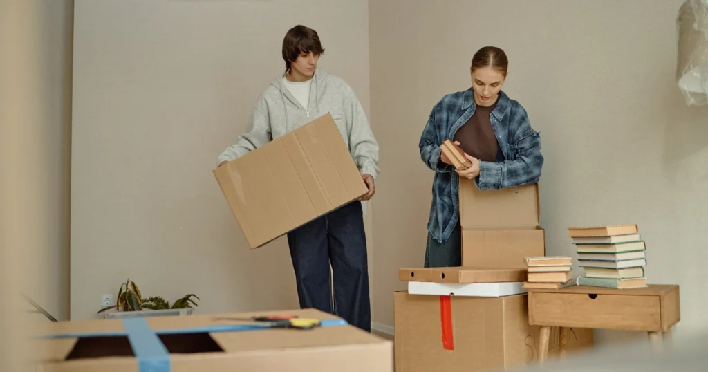 Two individuals carrying boxes into a room, demonstrating teamwork and organization during a move.